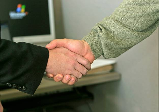 Landlord and tenant sitting with a neutral mediator in an office, shaking hands after resolving rental dispute