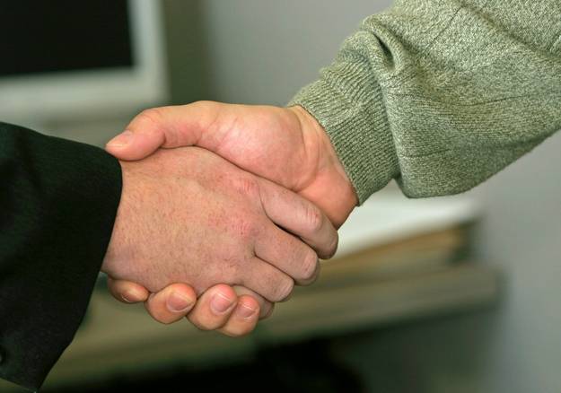 Landlord and tenant sitting with a neutral mediator in an office, shaking hands after resolving rental dispute